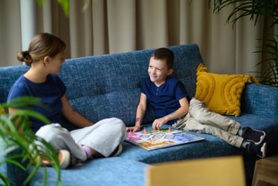 Brother and sister smiling and playing a fun board game together on a blue fabric sofa at Rodd Moncton