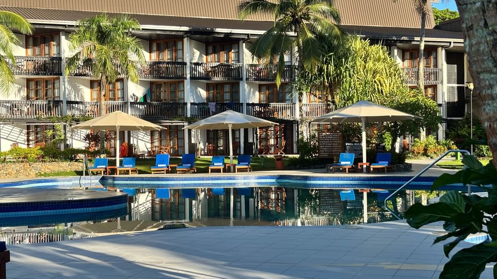 Swimming pool with lounge chairs under umbrellas at Warwick Fiji Resort and Spa in Korolevu.