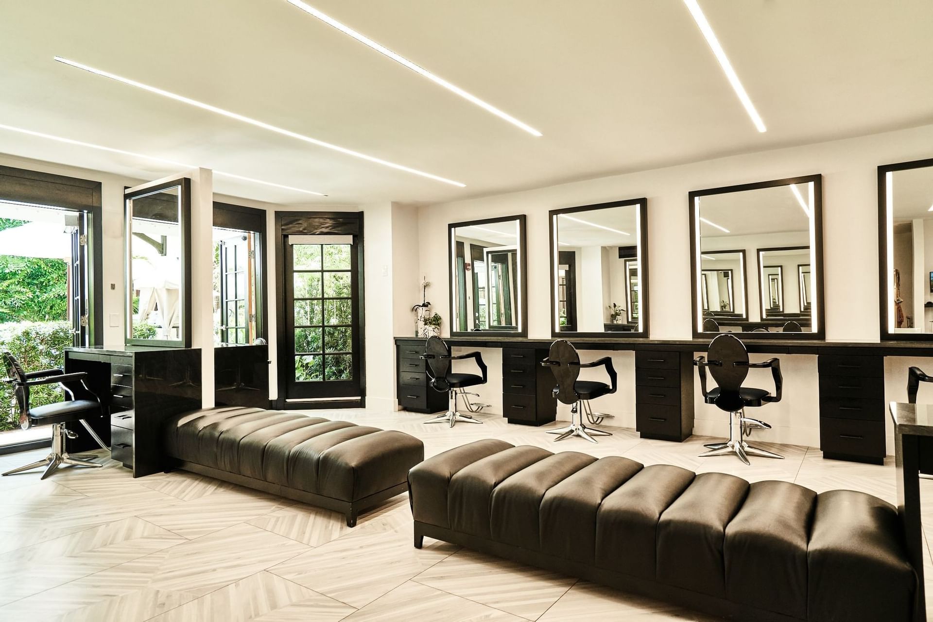 Styling stations with illuminated mirrors over long dark benches inside bright hair salon room at The Brazilian Court