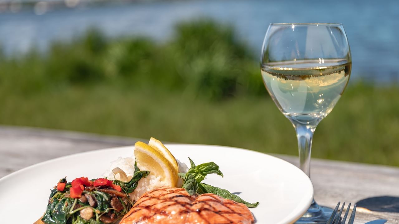 Salmon dish and white wine on outdoor table overlooking lake