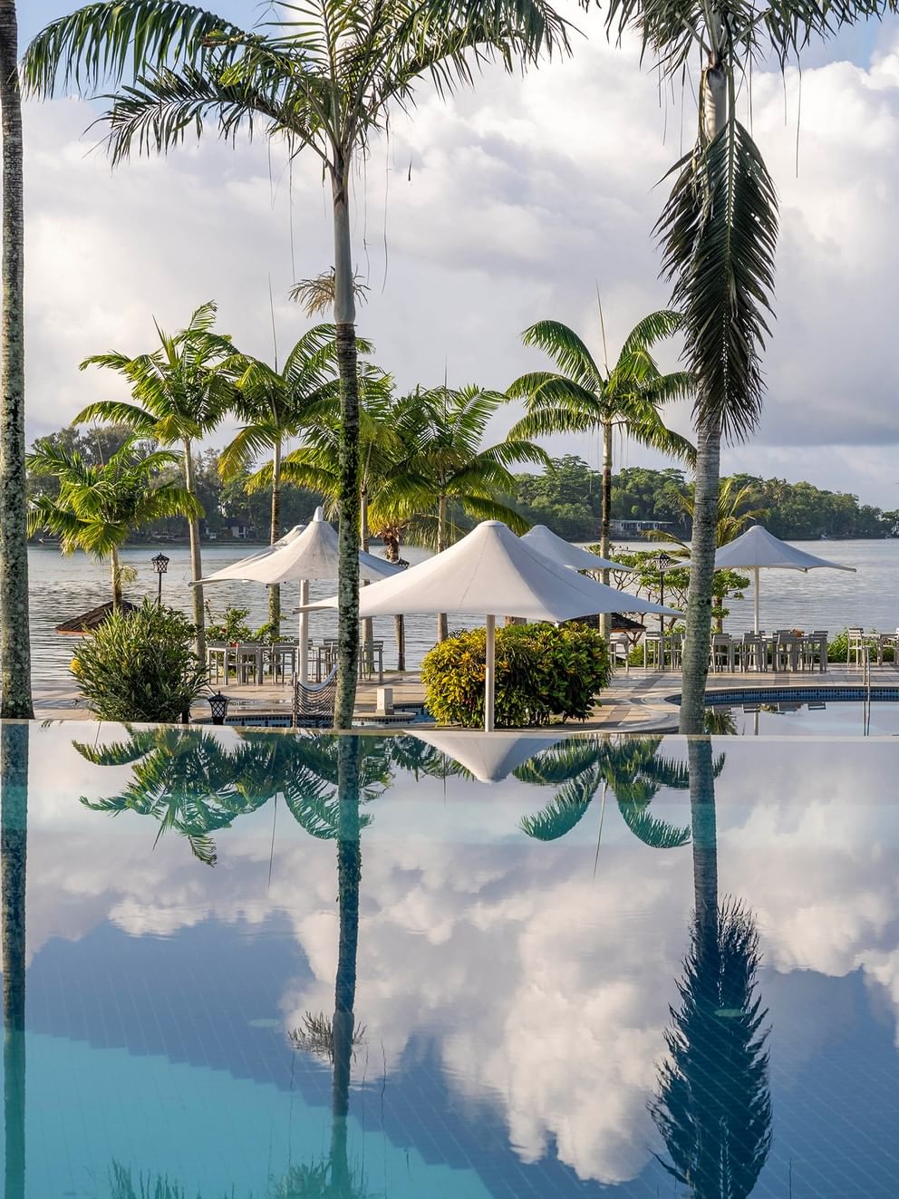 Serene pool with lounge chairs and umbrellas surrounded by lush palm trees at Warwick Le Lagon Vanuatu