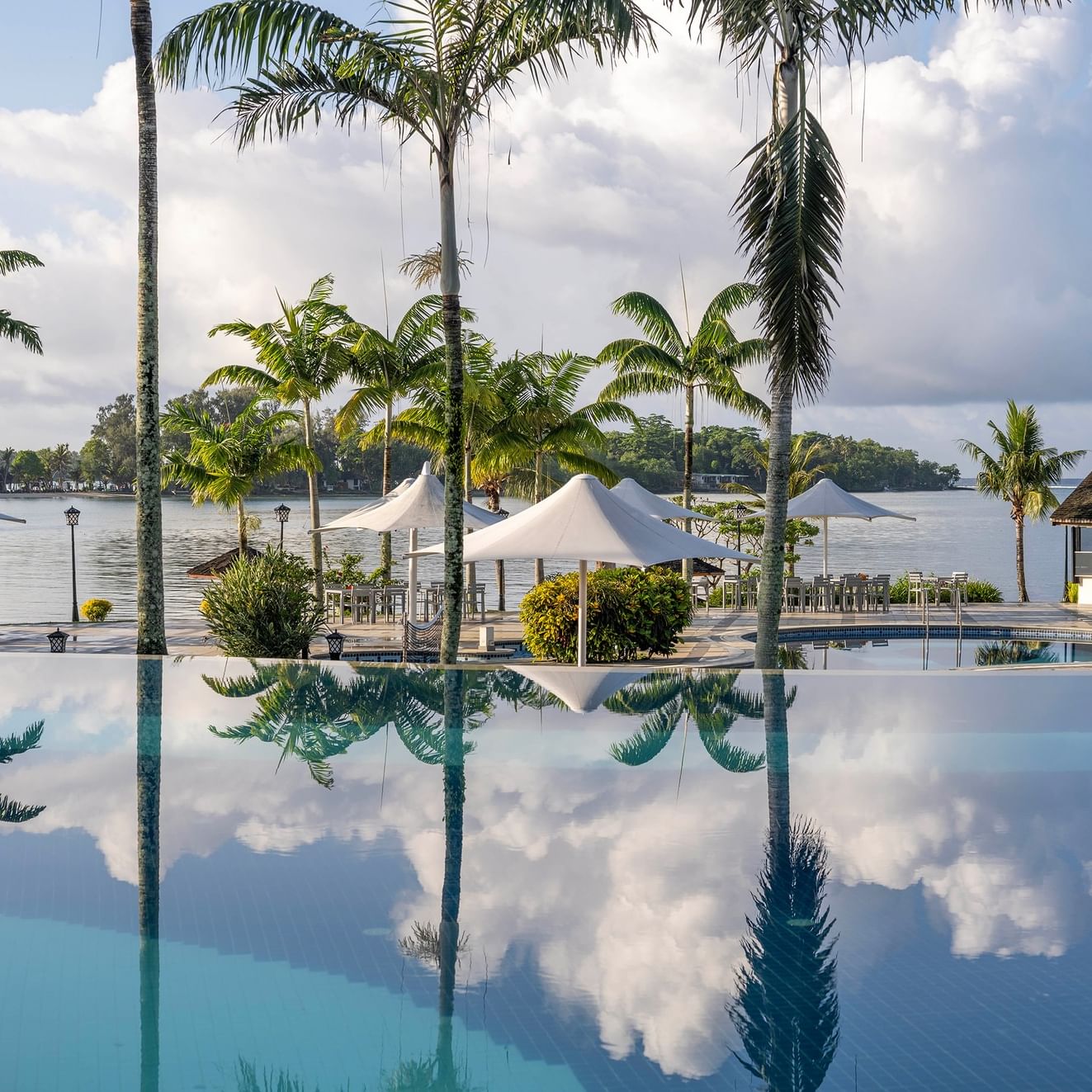 Une piscine paisible où se reflètent clairement les palmiers et les nuages, au Warwick Le Lagon - Vanuatu.