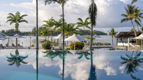 Serene pool with lounge chairs and umbrellas surrounded by lush palm trees at Warwick Le Lagon Vanuatu