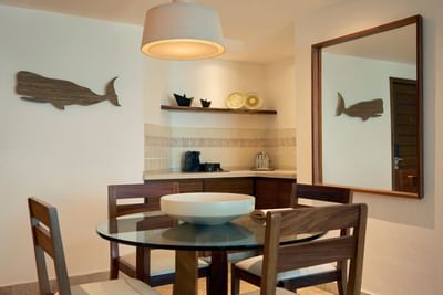 Dining area with glass table, four chairs, and decorative whale wall art, with a large mirror reflecting the room.