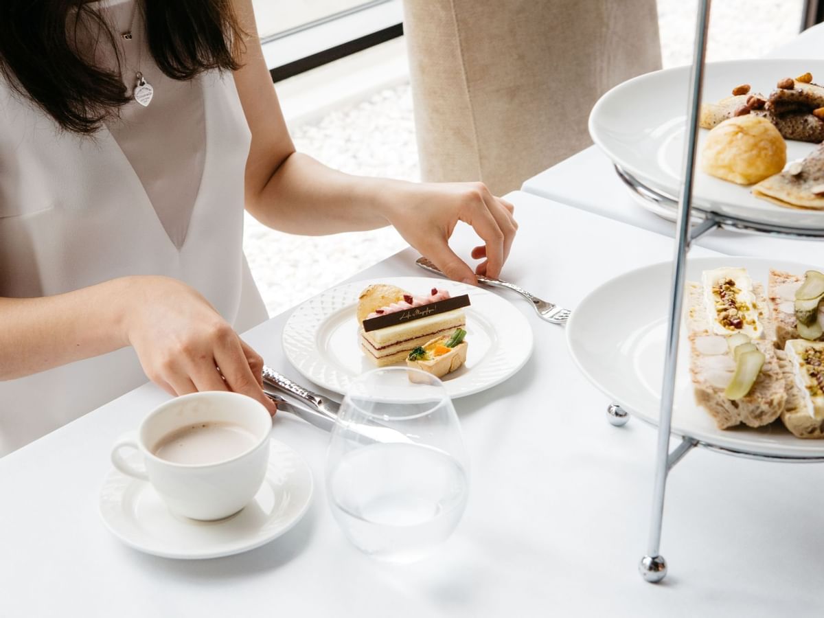 Person at a table with desserts, tea, and sandwiches, elegant afternoon high tea setting in Sofitel Brisbane Central
