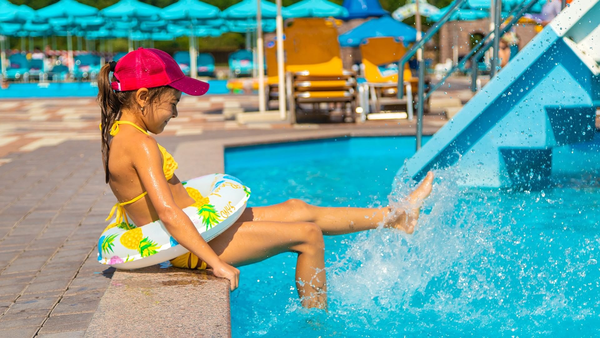 A young girl sitting on the edge of a pool with her feet in the water.