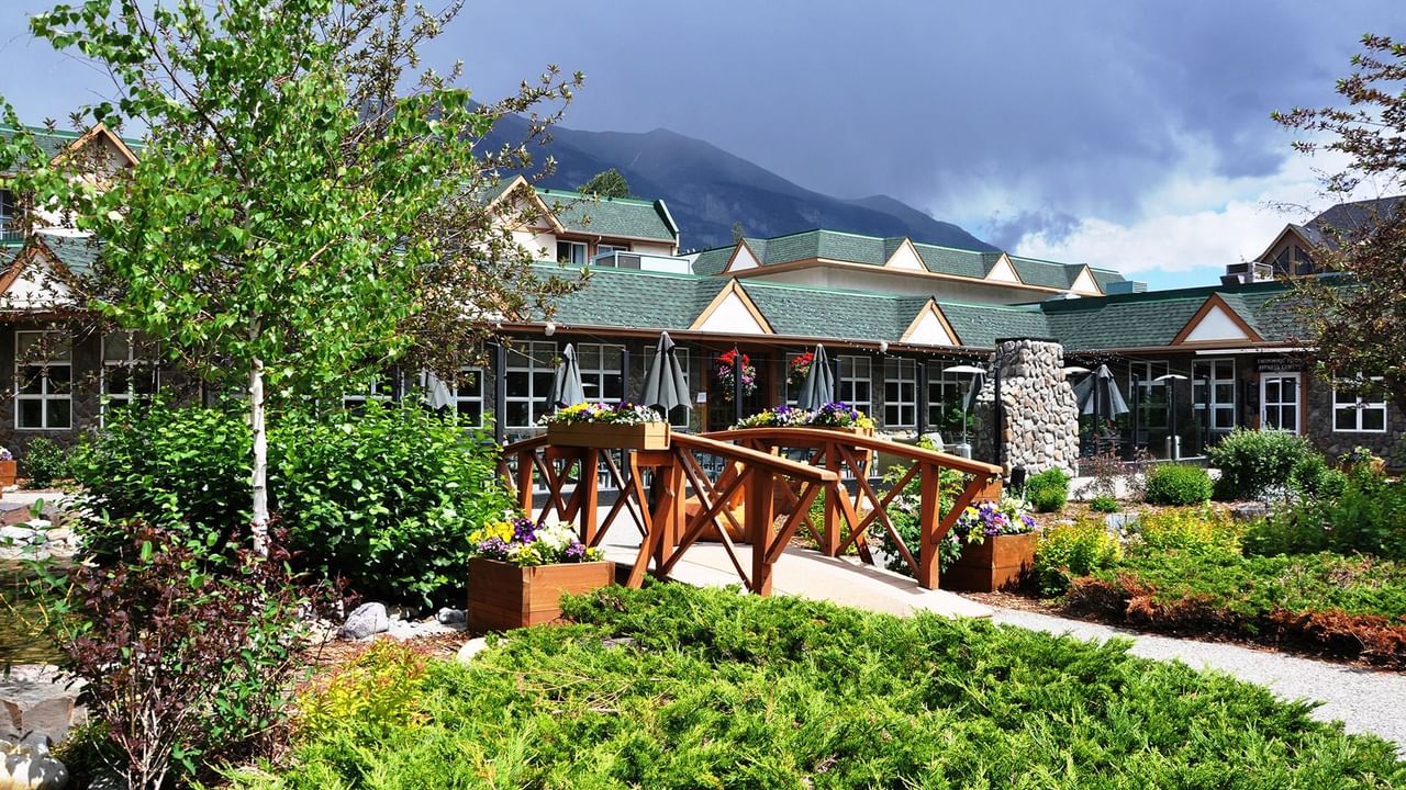 Coast Canmore Hotel surrounded by lush gardens and a wooden bridge