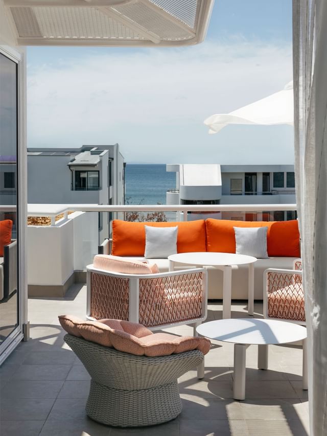 Ocean view balcony at Elysium Noosa with an orange sofa and woven chairs surrounding round tables under a white umbrella