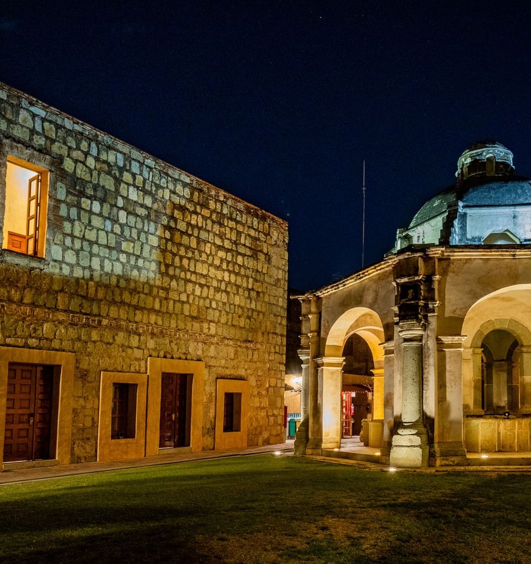 Edificio histórico de piedra y cúpula iluminada en jardín nocturno en Quinta Real Oaxaca