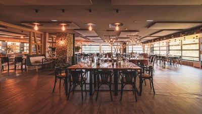 An empty restaurant with large windows, wooden floor, and multiple tables with chairs and glasses.