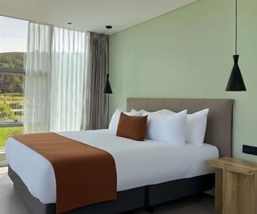 Guest room with a white bed and rust-colored runner by a large window at Unika Hotels, the best location to stay in Bogota