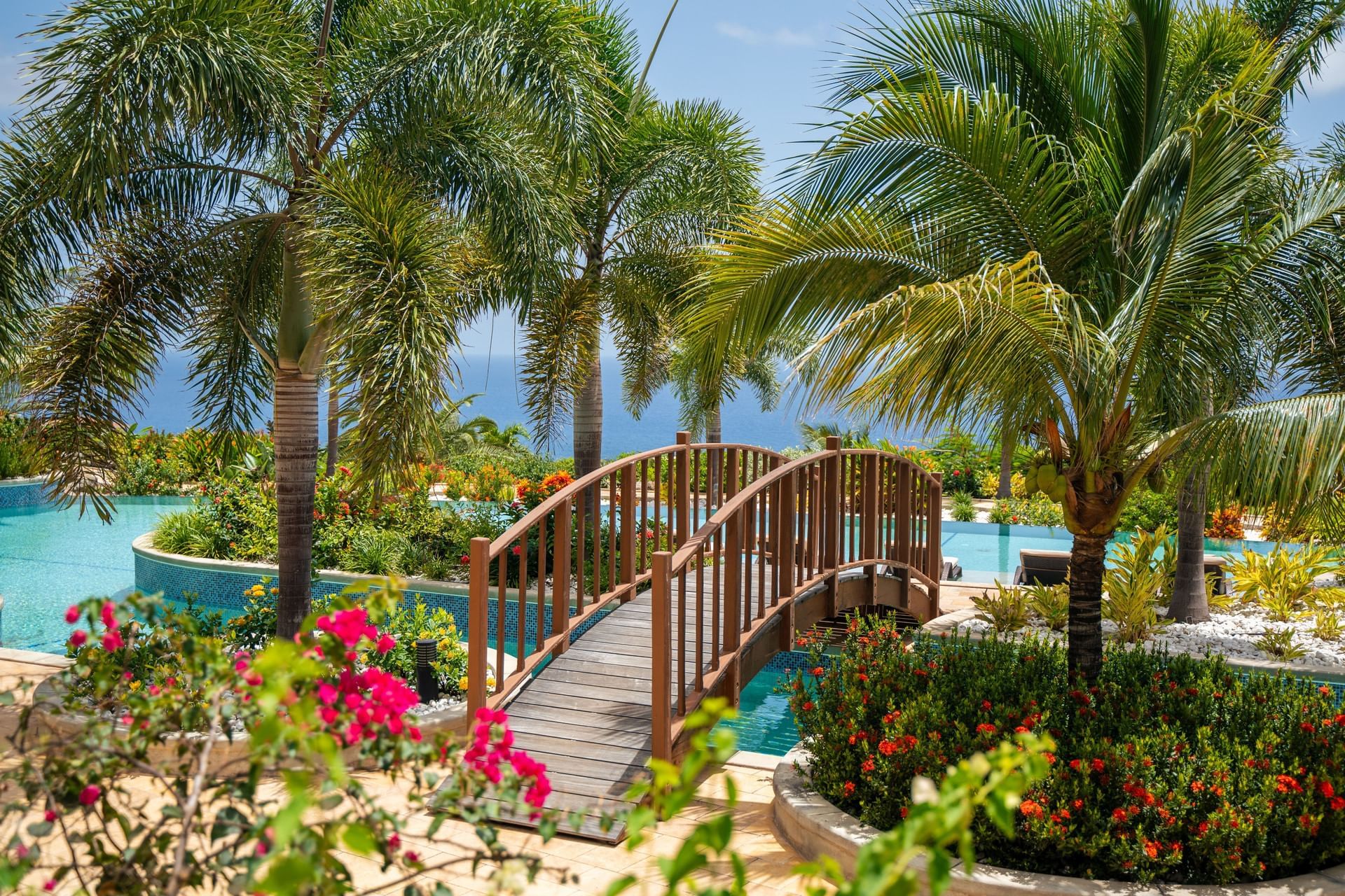Hummingbird Pool Bridge surrounded by lush palm trees and vibrant flowering plants at Golden Rock Resort