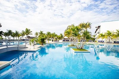 Large outdoor pool with island planters featuring palm trees and blue lounge chairs at Playa Blanca Beach Resort