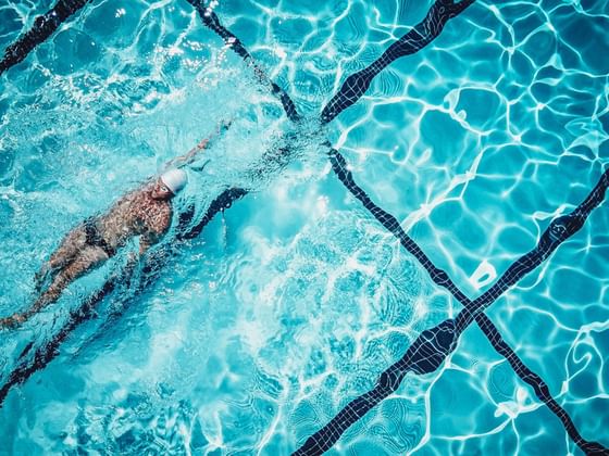 Top-down view of a swimmer in the Aquatic Center pool, diving through sparkling water at Hotel des Innovations