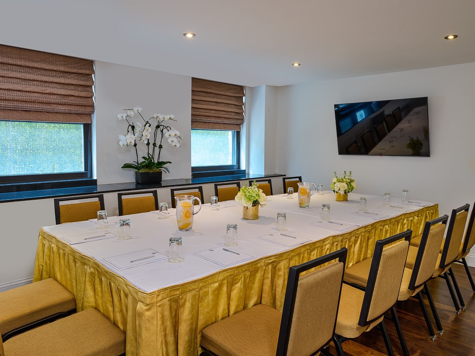 Conference table set surrounded by chairs facing the wall, TV & orchid plant in the Breakout Room at The Kimberly Hotel