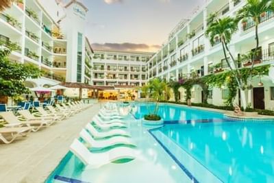 Outdoor pool surrounded by white lounge chairs and palm trees between hotel buildings at Playa Los Arcos Puerto Vallarta