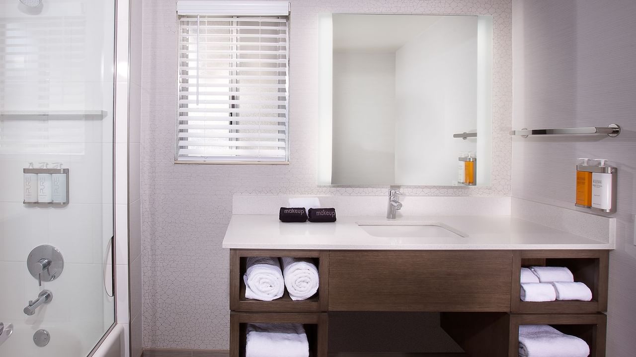Modern bathroom with glass shower, white sink, mirror, and cabinet with folded towels.