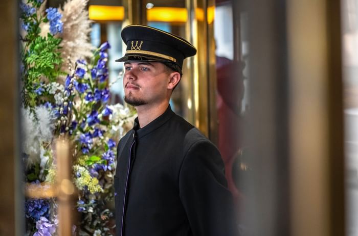 Bellhop in uniform by floral art under warm lights in the lobby at Warwick Paris Champs Elysées