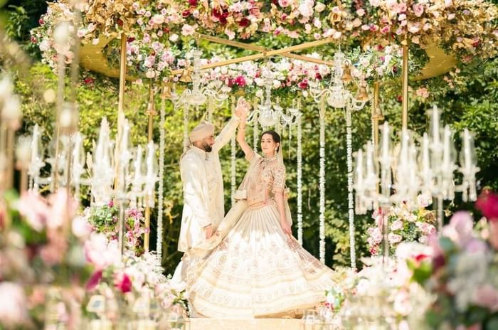 A couple beneath a floral mandap during an outdoor wedding ceremony in the grounds