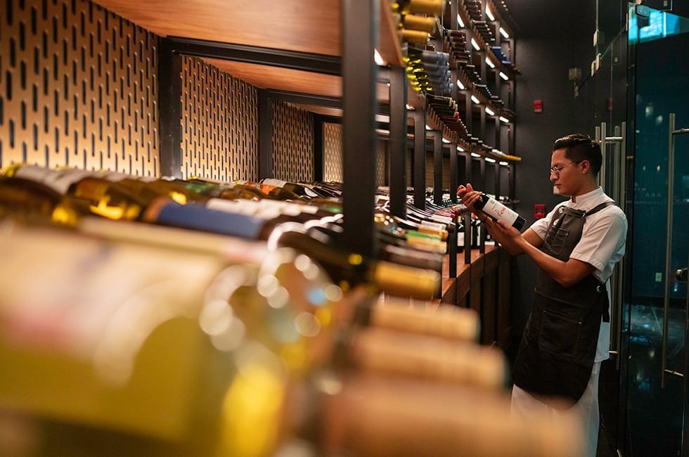 Person examining wine bottles in a dimly lit cellar with racks of wine at Live Aqua Resorts and Residence Club