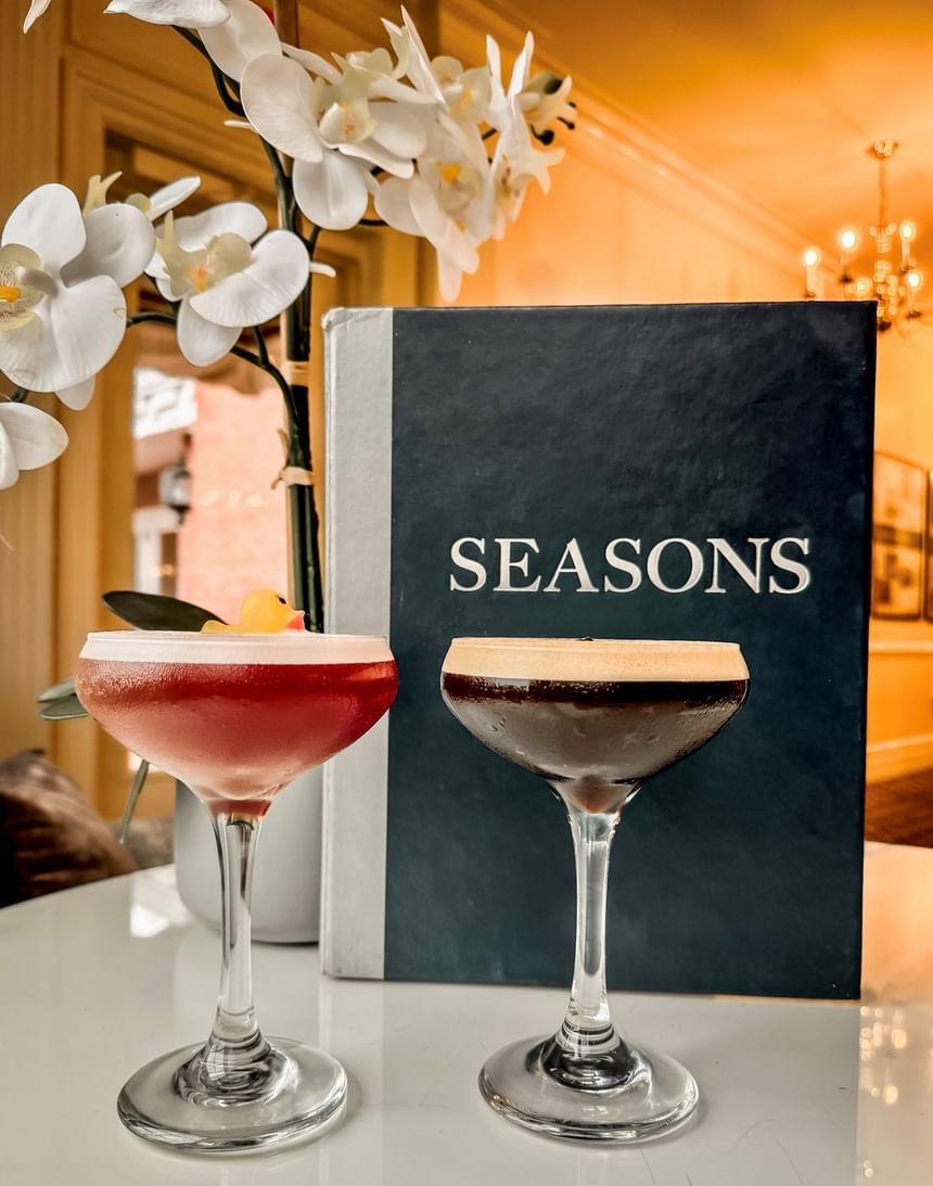 Two cocktail glasses filled with drinks set on a table near the menu book in the dining space at Avon Old Farms Hotel