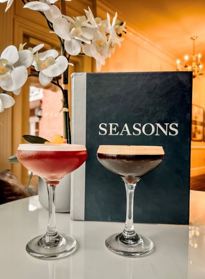 Two cocktail glasses filled with drinks set on a table near the menu book in the dining space at Avon Old Farms Hotel