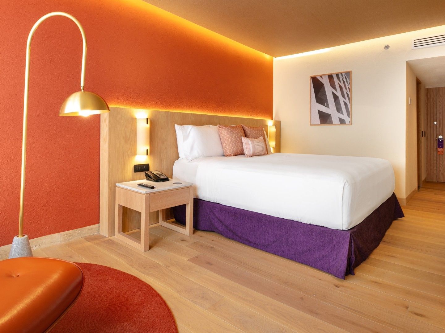 King Deluxe Plus room with a bold orange accent wall, wood flooring, and stylish gold lamp at Camino Real Polanco Mexico
