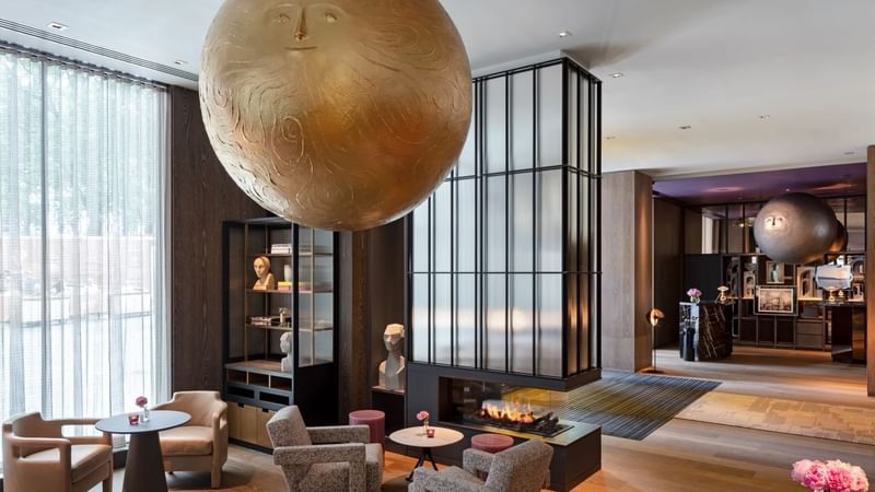 Elegant hotel lobby featuring a sun and moon head art installation, modern seating, and sculptural displays at The Londoner Hotel