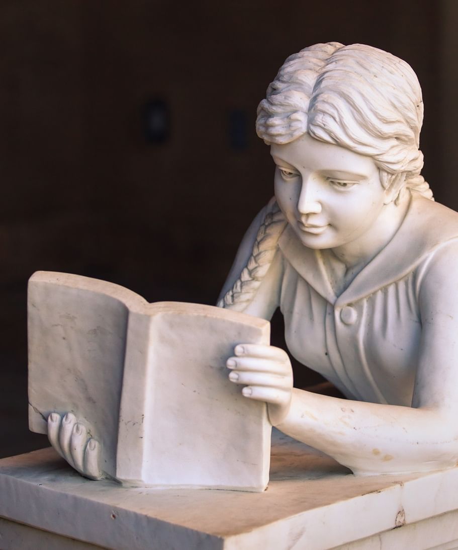 Stone sculpture of a women laying on her stomach reading