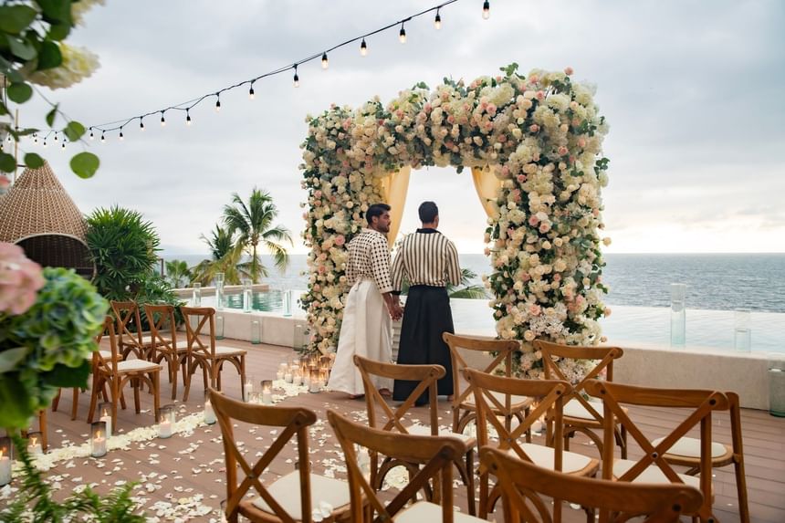 Two grooms holding hands under a floral arch during an oceanfront wedding ceremony at Almar LGBT Luxury Resort