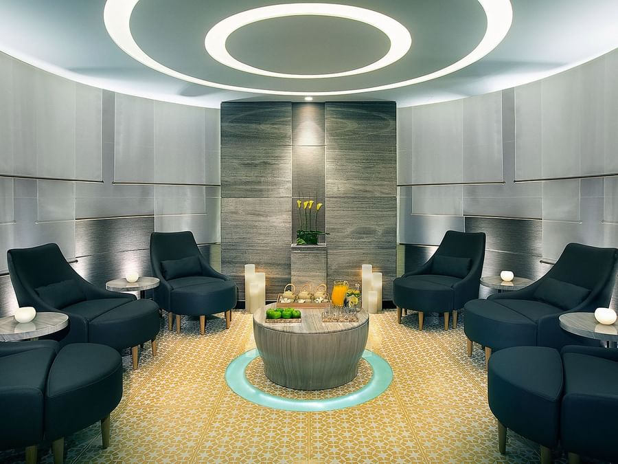 Modern lounge area with black chairs, circular ceiling light, and a wood centerpiece table in a spa at DAMAC Hotels & Resorts