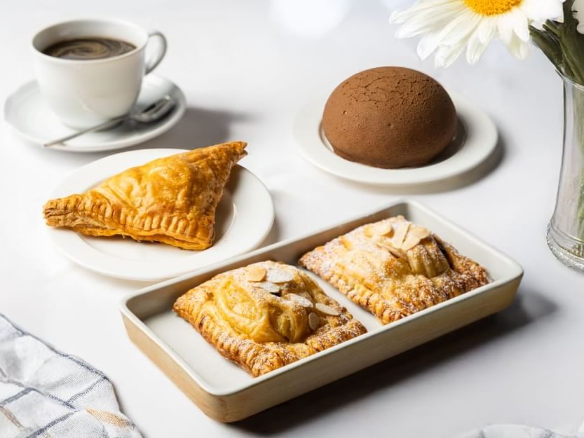 A white table displays a plate of pastries, a cup of coffee, and a vibrant flower centerpiece.