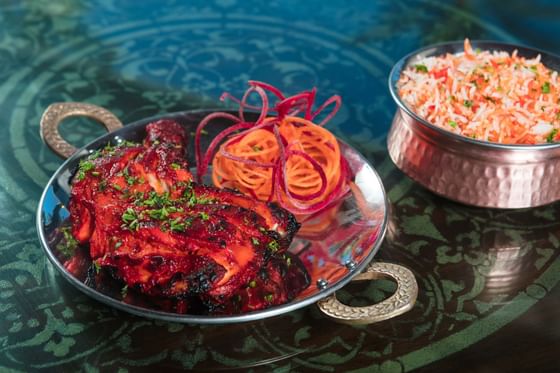 A plate of tandoori chicken next to a bowl of biryani served on a table at All Seasons Resort Europa