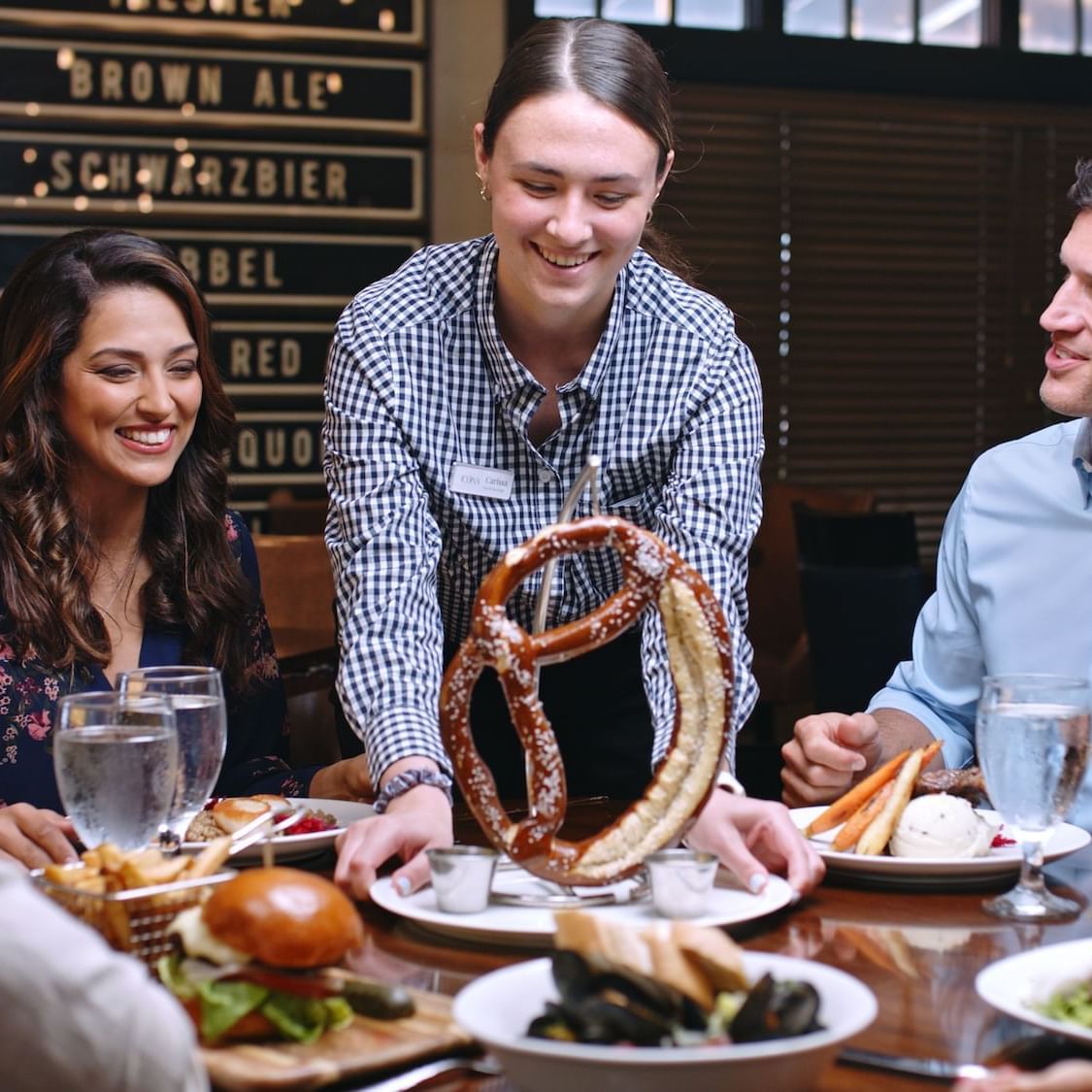 couples enjoying dinner at Avalon Brew Pub, server is smiling and presenting a giant Bavarian pretzel to the table