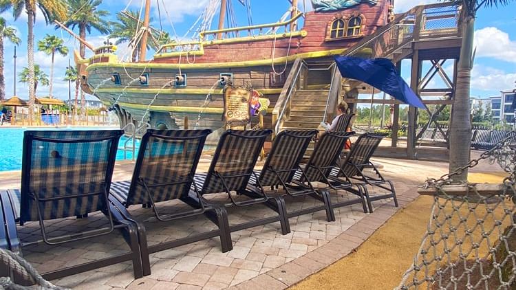 A poolside area with lounge chairs and a pirate ship in the background.