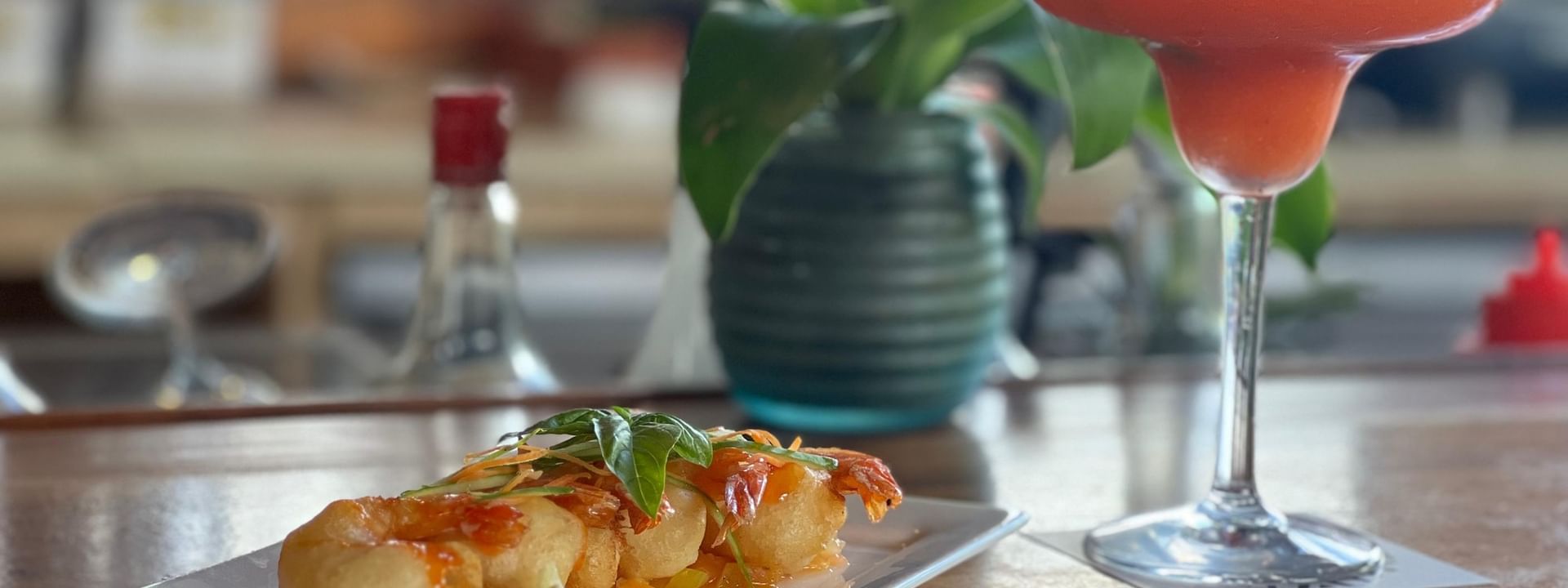 Plate of fried shrimp and a red cocktail by a small potted plant in KanaVata Restaurant at TokaToka Resort Nadi Fiji