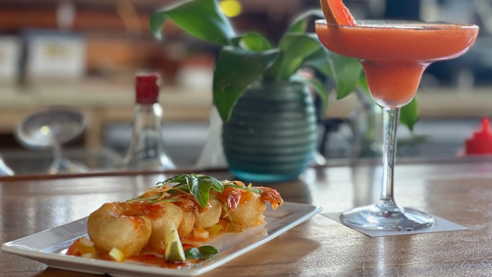 Plate of fried shrimp and a red cocktail by a small potted plant in KanaVata Restaurant at TokaToka Resort Nadi Fiji