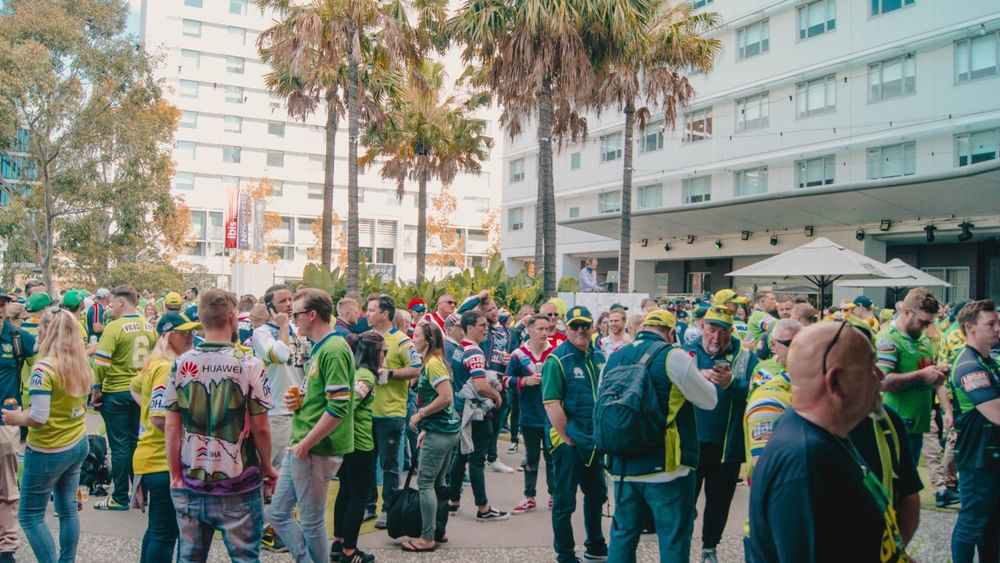 Sports fans in green and blue jerseys gather outdoors at the Novotel Sydney Olympic Park
