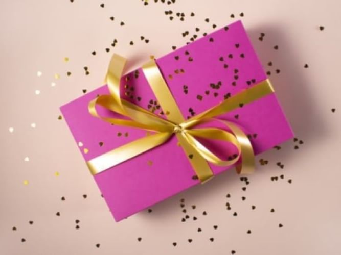 A closeup picture of a purple gift tied from a gold ribbon