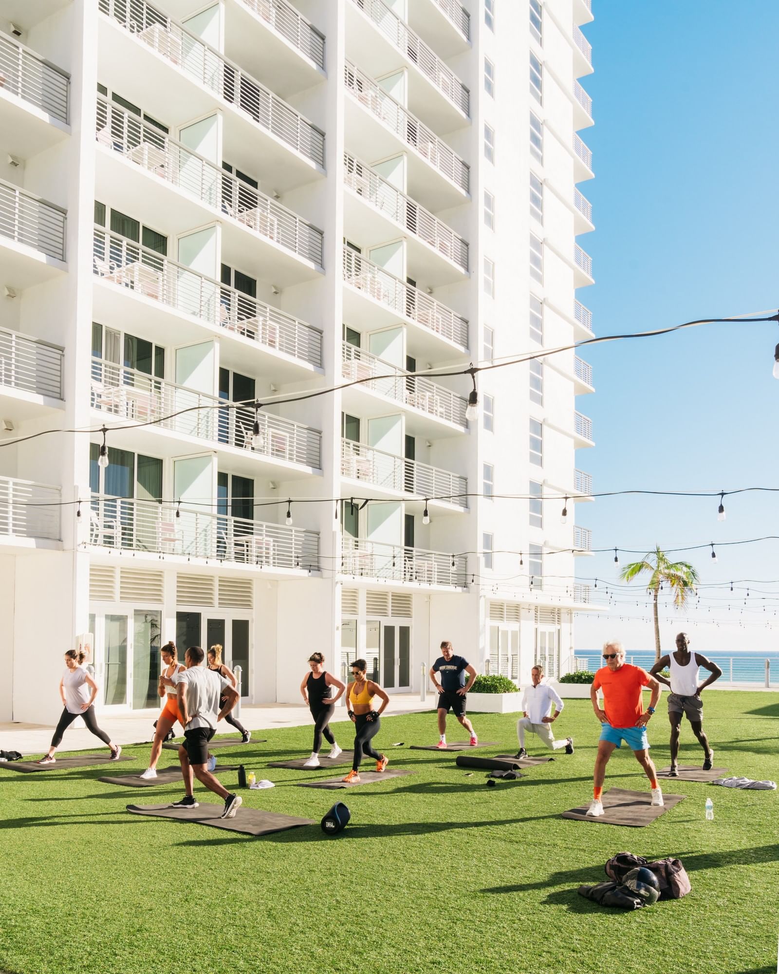 A group of people doing yoga on exercise mats in a grassy area in front of a large white building.