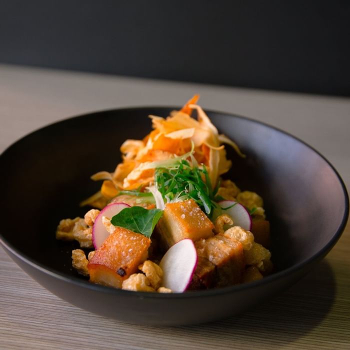 Delicious dish featuring crispy fried pork belly, fresh radish, and herbs, served at Ibis Adelaide