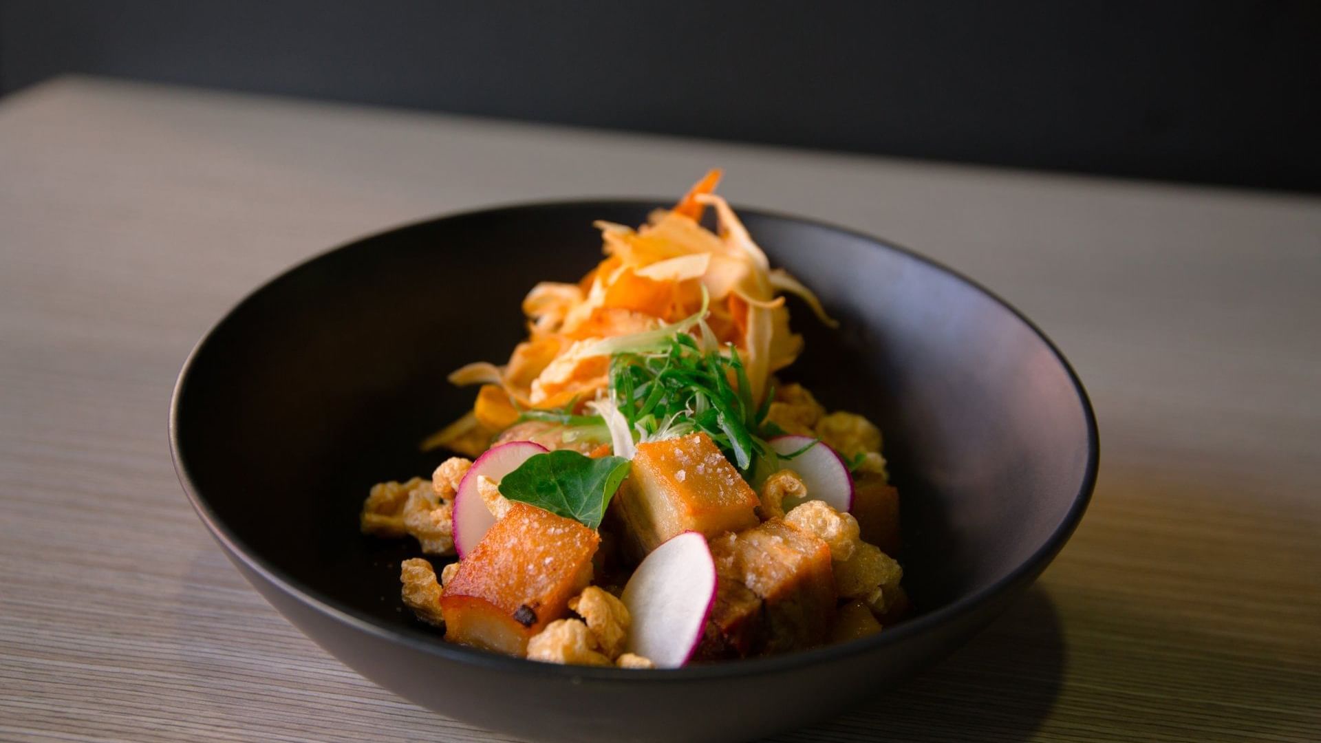 Delicious dish featuring crispy fried pork belly, fresh radish, and herbs, served at Ibis Adelaide