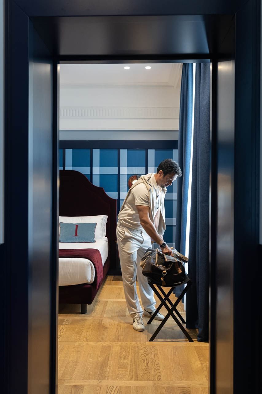 Person looks into a large bag in Cielo Suite, with a bed and blue accent wall at The Independent