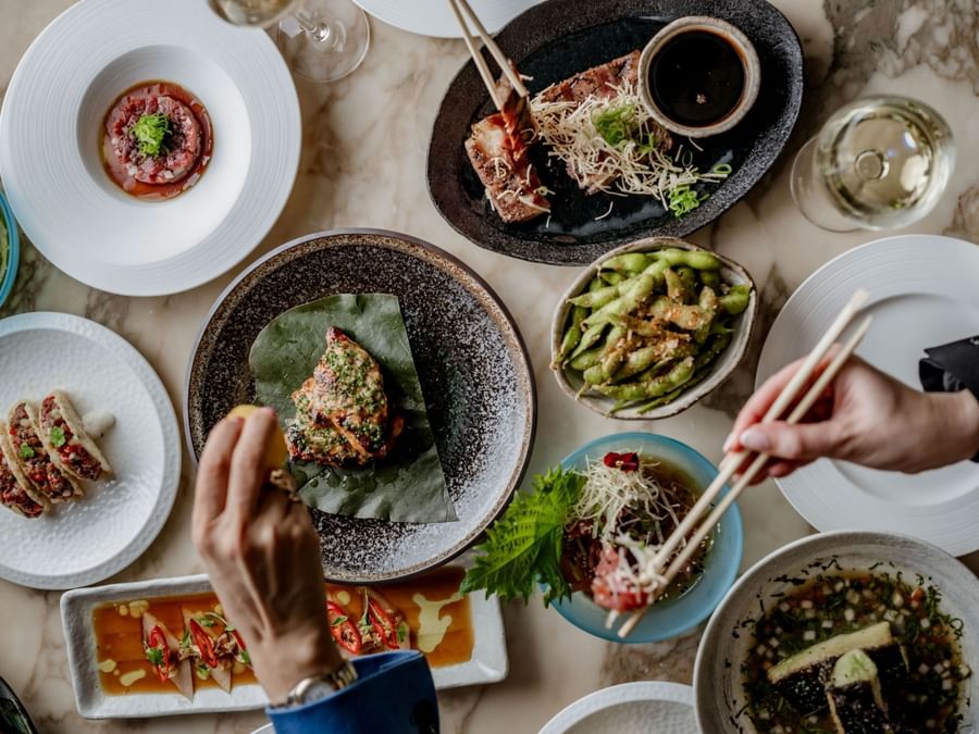 Overhead view of Asian dishes on a table with two people sharing the meal using chopsticks at The May Fair Hotel