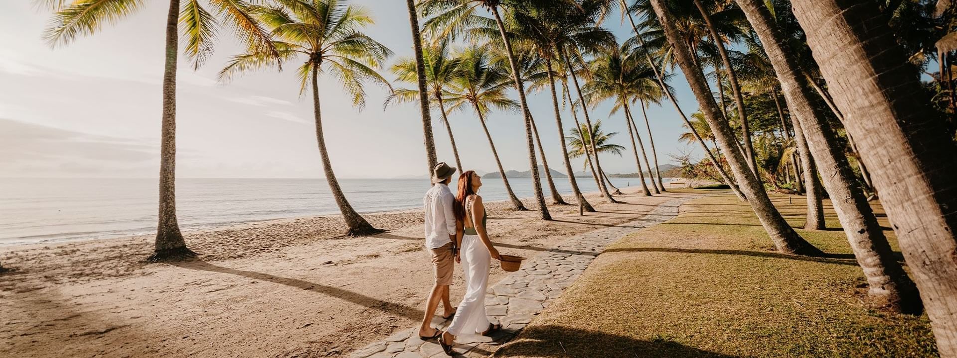 A couple holding hands while walking along a path next to the beach near Pullman Palm Cove Sea Temple Resort & Spa