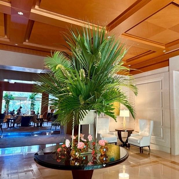 Elegant lobby featuring a dramatic tropical palm arrangement with pink roses and decorative elements on a round table.