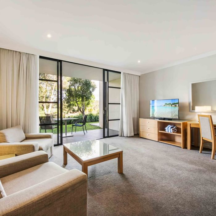 One Bedroom Apartment living room with sofas, sliding door to the garden, and a television at Mercure Kooindah Waters