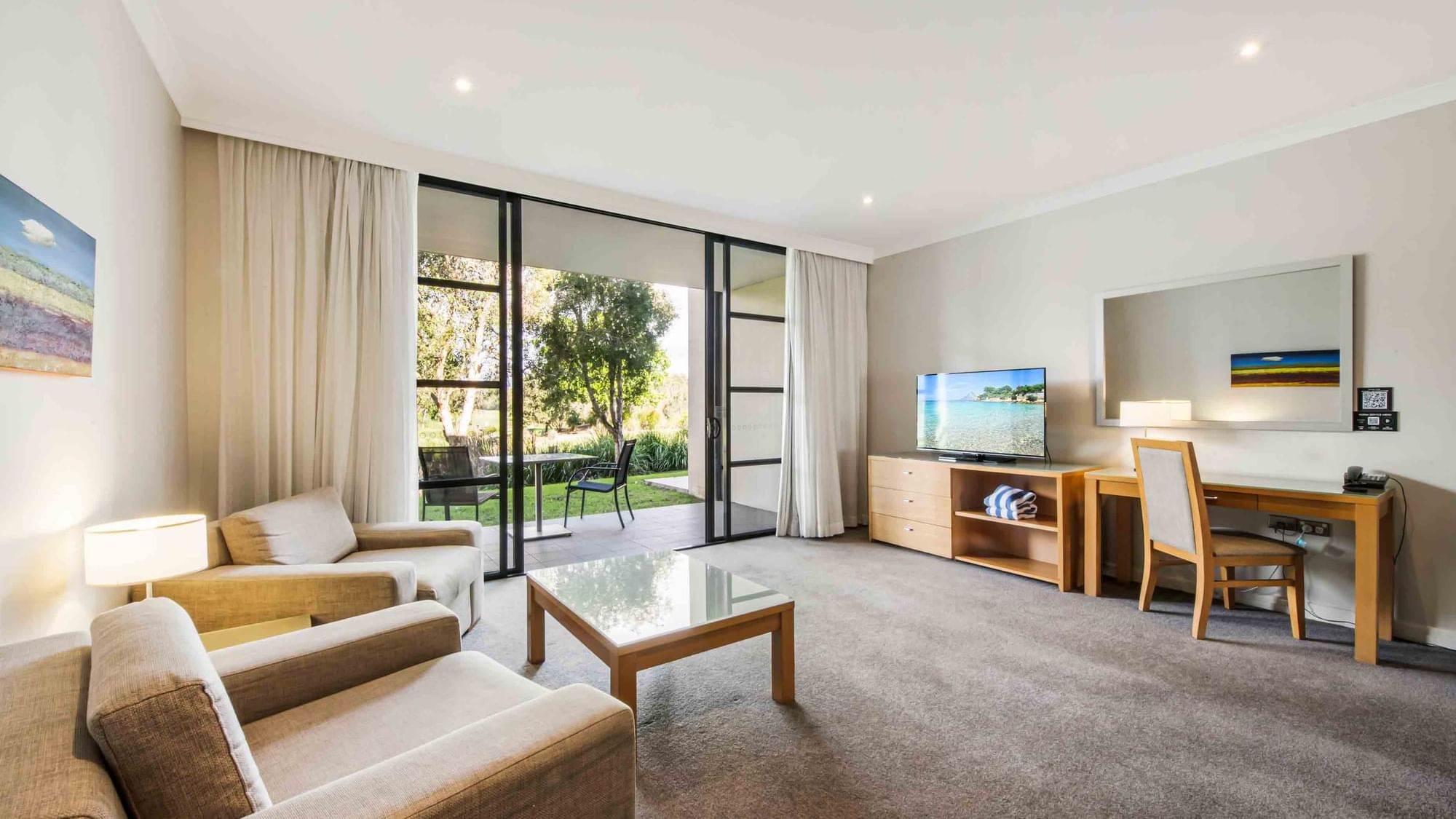 One Bedroom Apartment living room with sofas, sliding door to the garden, and a television at Mercure Kooindah Waters