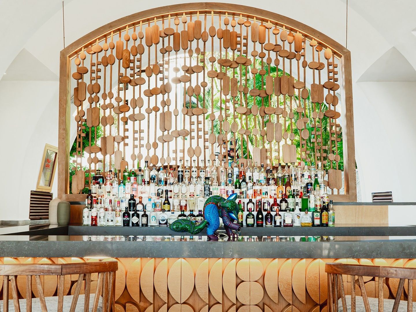 Bar counter with a carved wood facade and illuminated bottle shelf in Bitza Lounge Bar at Camino Real Zaashila Huatulco