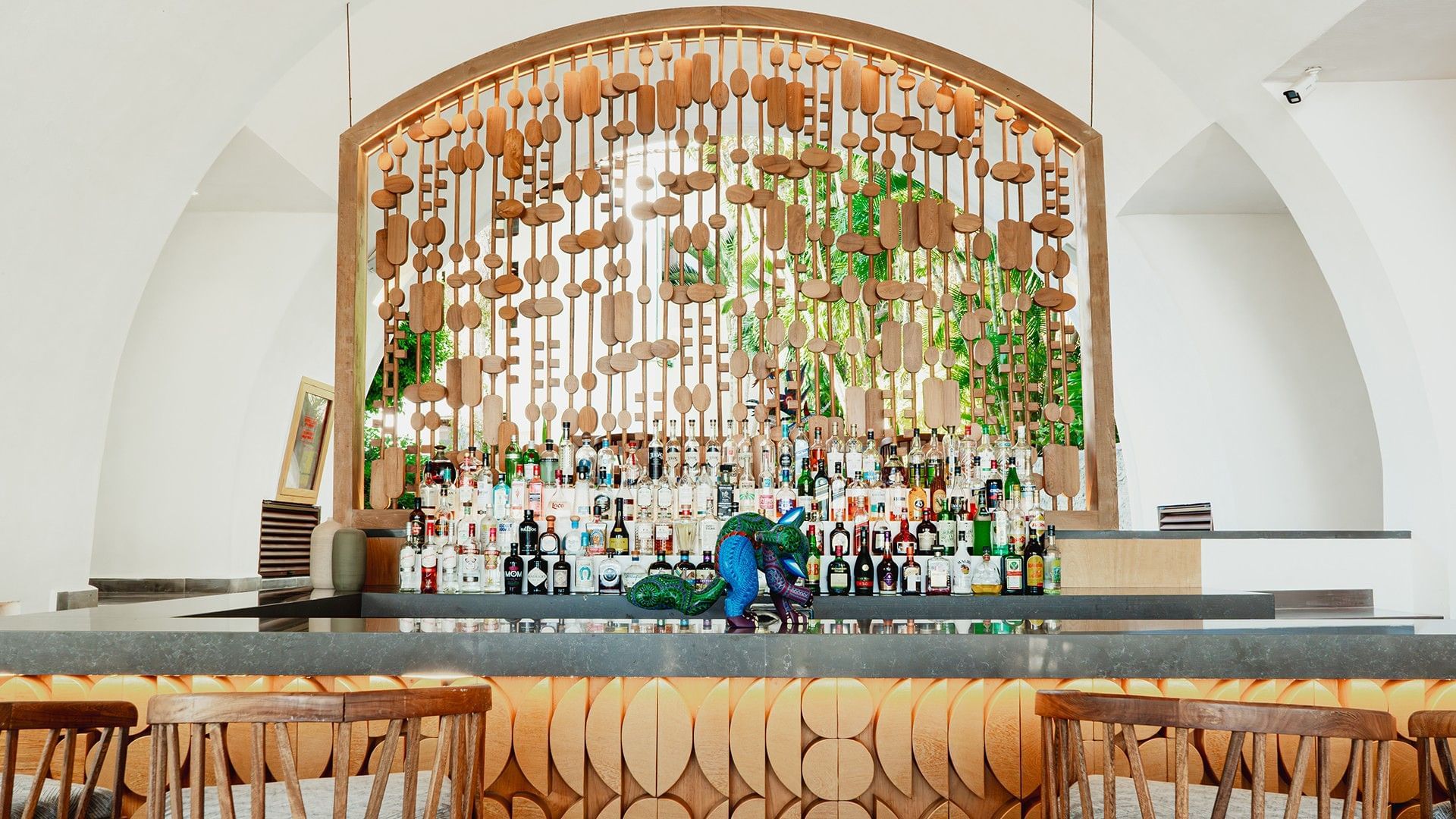 Bar counter with a carved wood facade and illuminated bottle shelf in Bitza Lounge Bar at Camino Real Zaashila Huatulco